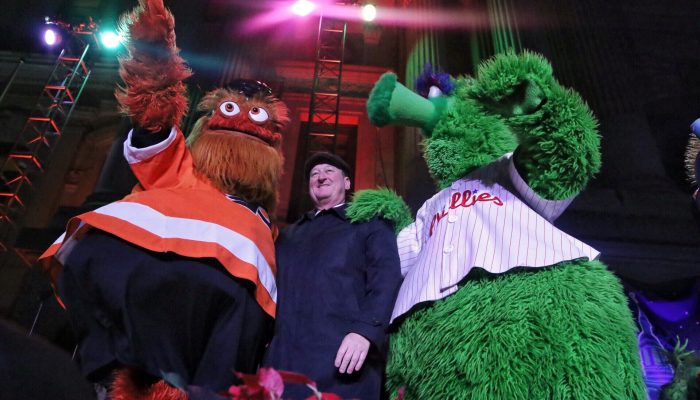 Flyers masdcot Gritty and the Phillie Phanatic standing next to Mayor Kenney at City Hall's holiday tree lighting in 2018.