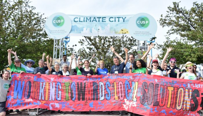 Representatives from local environmental organizations gather at CUSP's Climate City. The group holds a sign that reads "Working Towards Local Solutions"