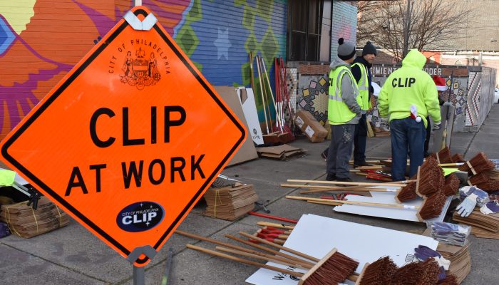 Workers outside with cleaning tools behind a traffic sign.