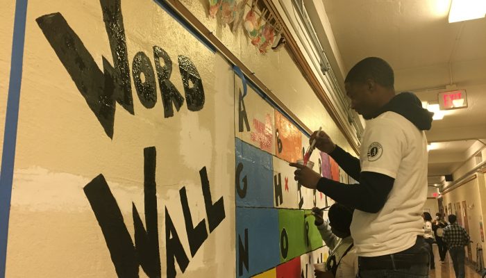 A volunteer paints a mural in progress at F.S. Edmonds Elementary School that reads "Word Wall"