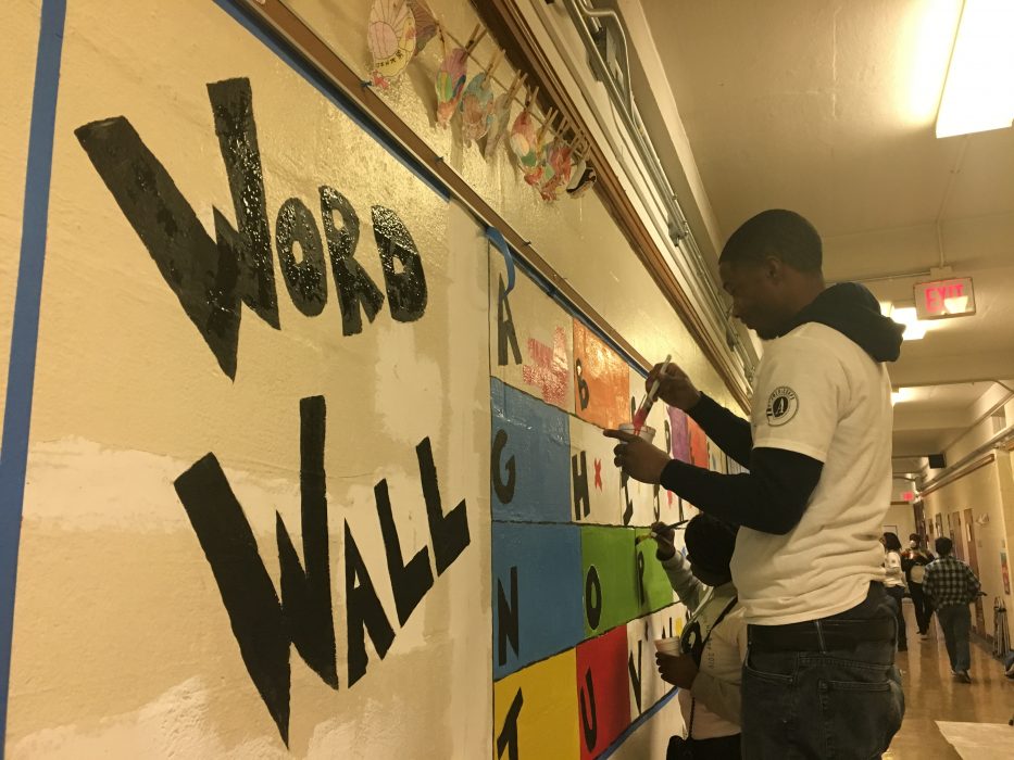 A volunteer paints a mural in progress at F.S. Edmonds Elementary School that reads "Word Wall"
