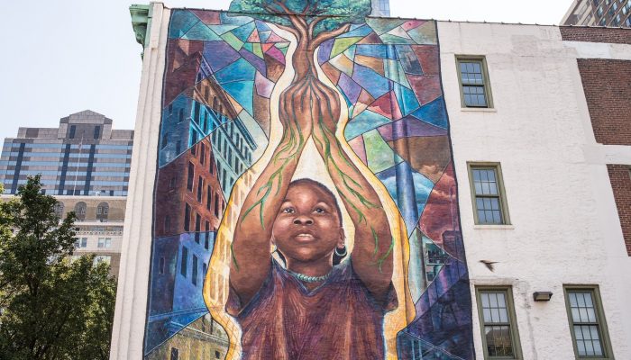 mural of young black girl holding a tree in her hands with the roots as part of her veins