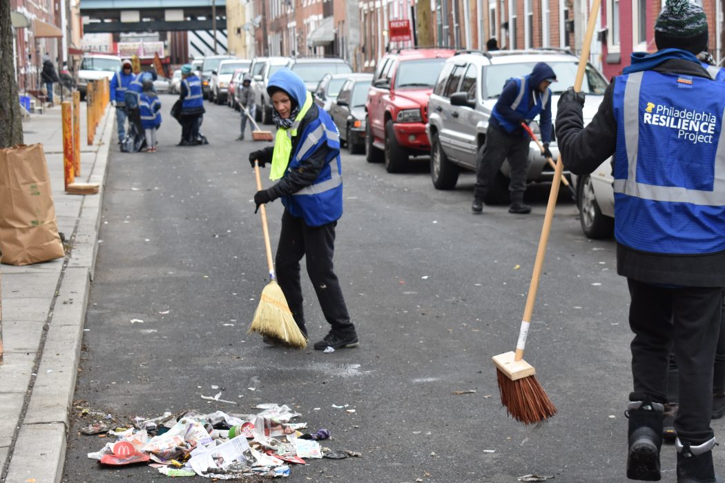A volunteer sweeping a street on a Kensington neighborhood block.