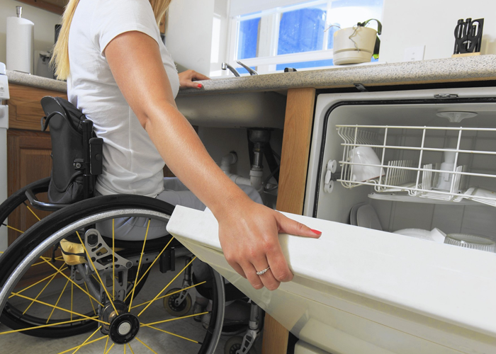 A woman in a wheelchair closes a dishwasher.