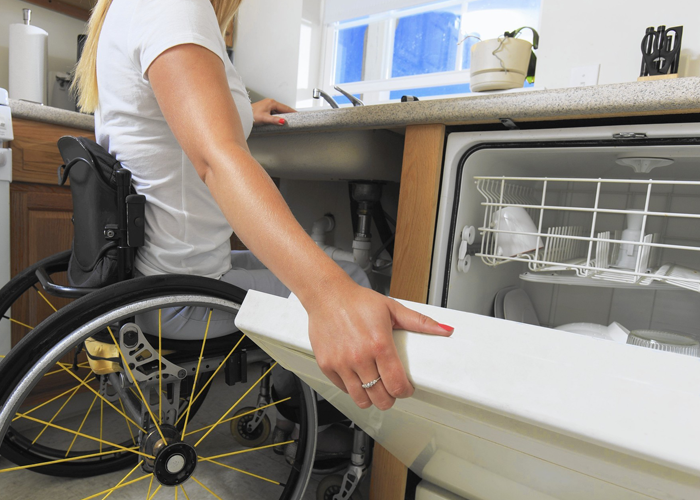 Une femme en fauteuil roulant ferme le lave-vaisselle.