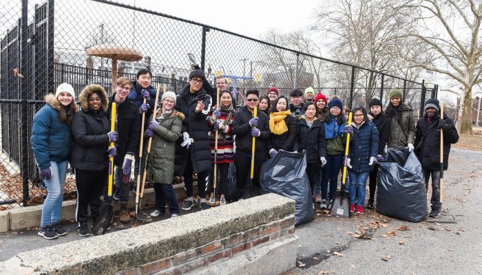 Group of people holding cleaning supplies and standing next to trash bags after a cleanup