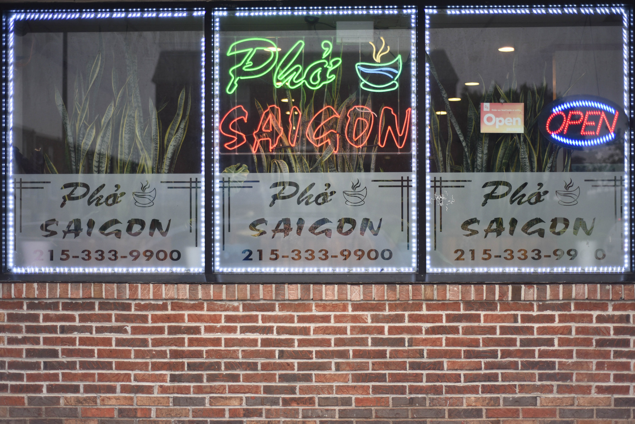 The brick exterior of Pho Saigon. The windows feature a neon sign.