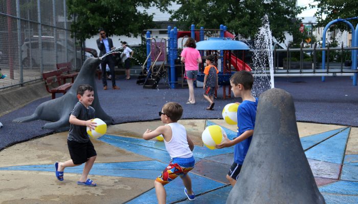 Kids running and playing with inflatable beach balls on a playground with a water-spray feature