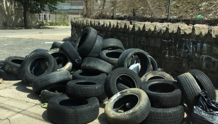 large pile of more than 20 tires that is blocking part of a sidewalk