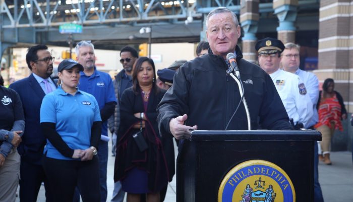 Mayor Kenney speaks at a podium outside while surrounded by community members and City officials