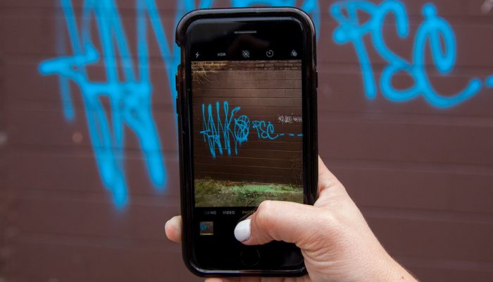 person holding up a phone and taking photos of graffiti to report it