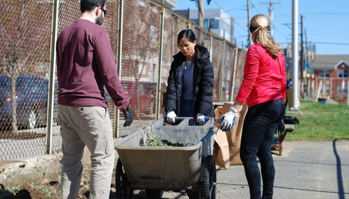 three people gathered around a wheelbarrow with gardening gloves on