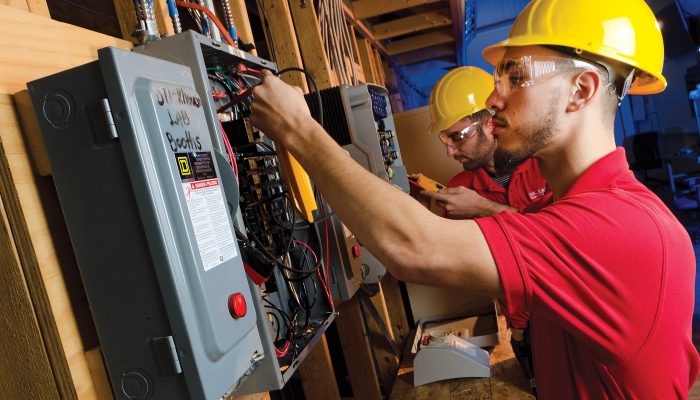 Workers in hard hats work on electrical boxes