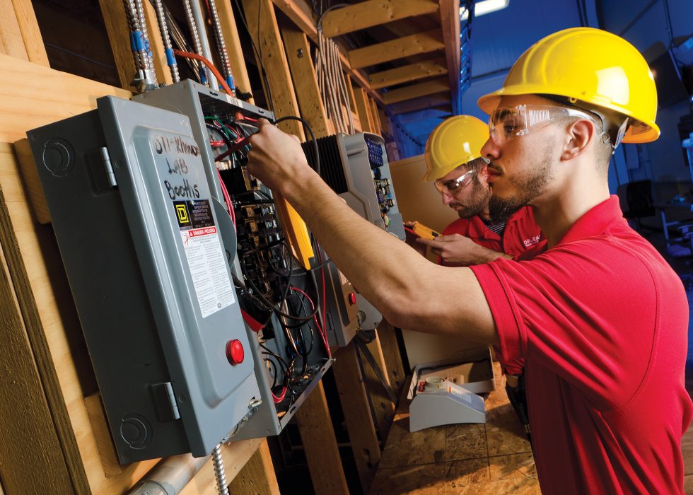 Workers in hard hats work on electrical boxes