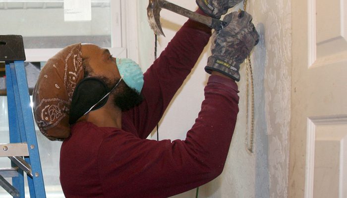 Man wearing a dust mask drives a nail with a hammer.