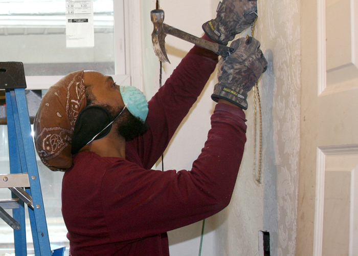 Man wearing a dust mask drives a nail with a hammer.