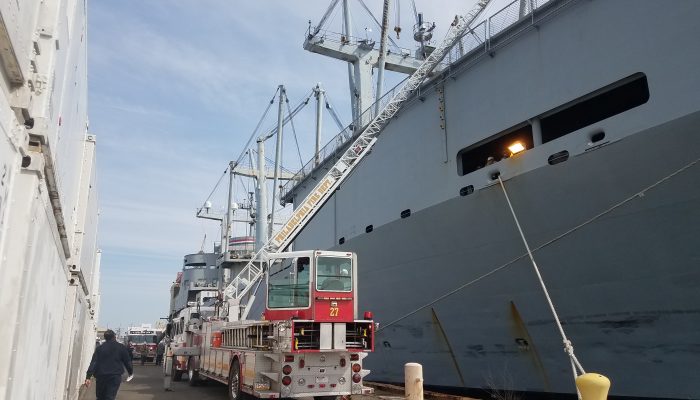 Fire truck parked on pier near large ship