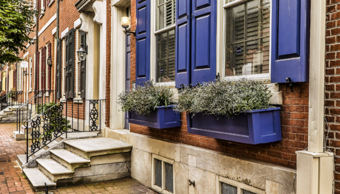 A brick row-home in Philadelphia with lush flowers potted underneath the home's windowsills.