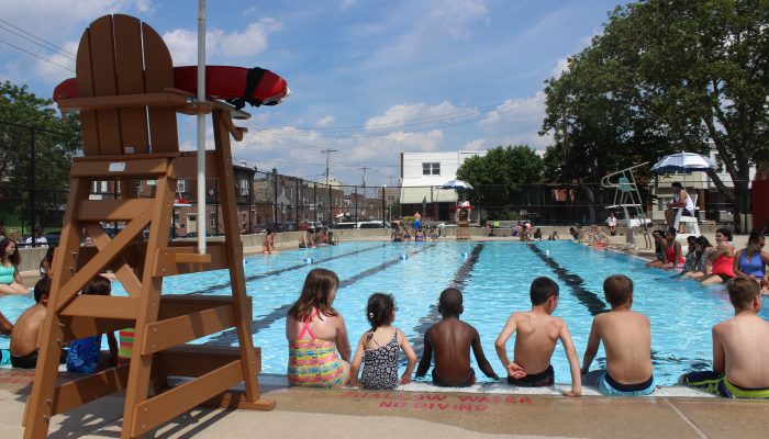 The backs of children sitting on a pool deck