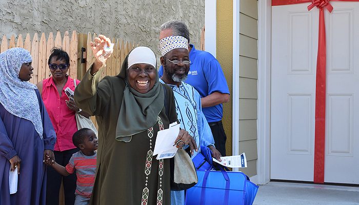 Une femme sourit et tient les clés en main alors qu'elle se tient devant sa première maison avec sa famille.