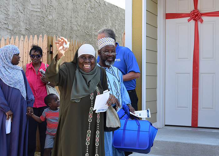 A woman smiles and holds up keys while standing in front of her first home with her family.