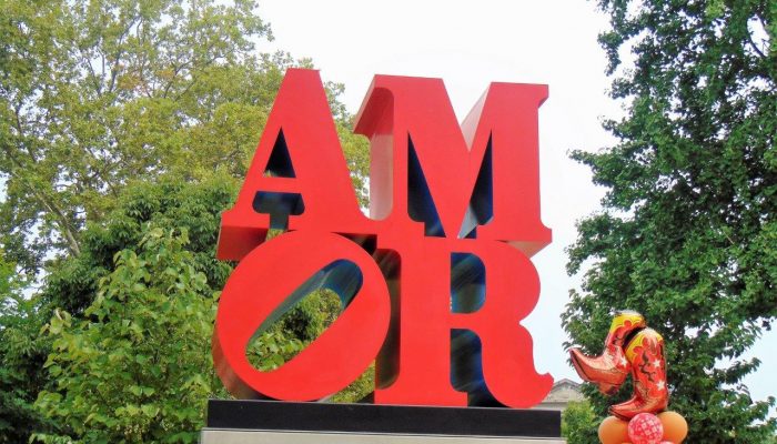 Red "Amor" statue with trees in the background.