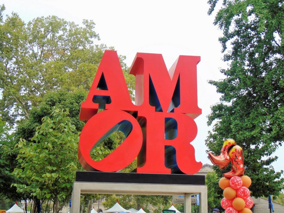 Red "Amor" statue with trees in the background.