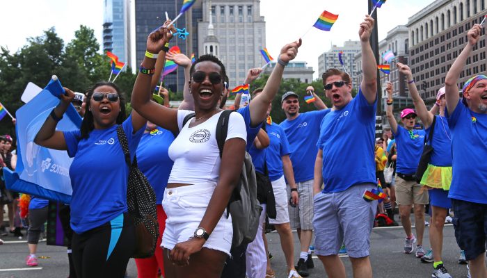 Group of people wearing blue shirts, waving small flags in LGBTQ Pride parade.
