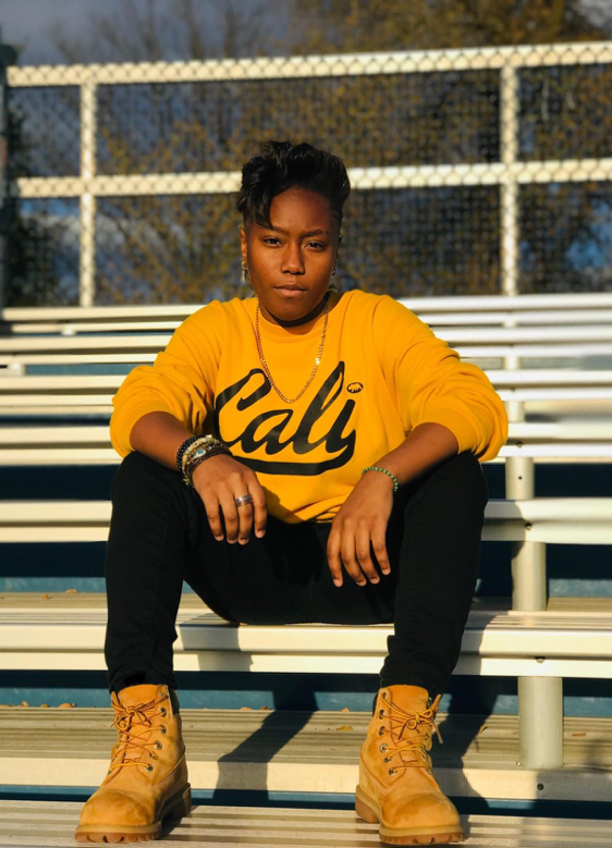 Person sitting on bleachers and wearing a yellow shirt, black pants, and construction boots. 