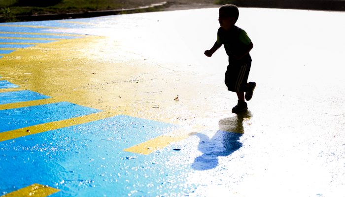 small child running across a painted blacktop in the sun