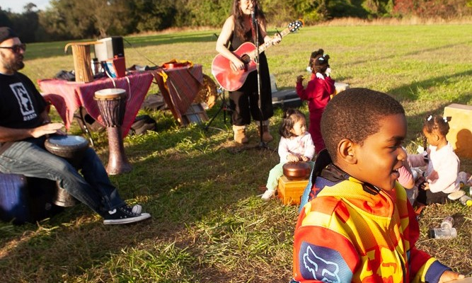 Woman playing guitar in a park with children watching.