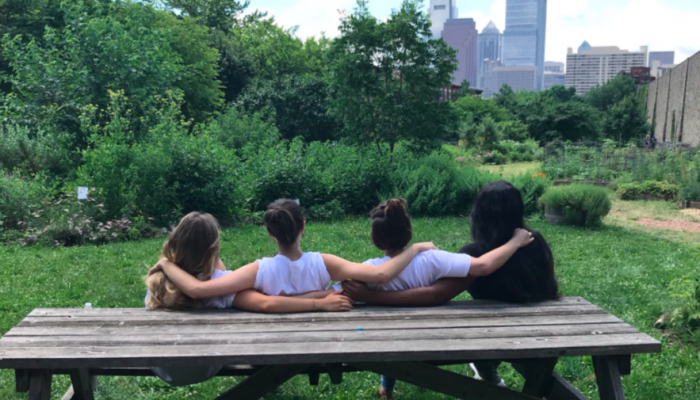 four youth with their backs to the camera sitting at a picnic bench with their arms around each other looking at the skyline of philadelphia