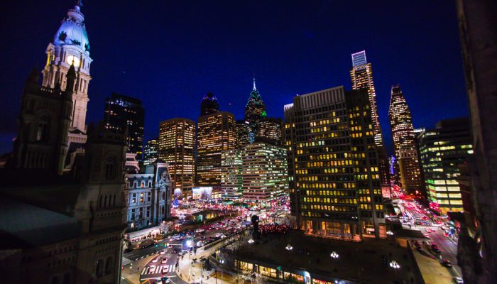 photo of philly skyline at night. Part of City Hall and surrounding buildings. Sky is deep blue and fades to black on outer edges of photo