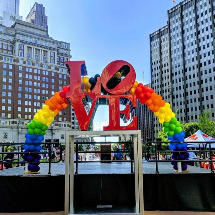 LOVE statue with rainbow balloon arch in the background.