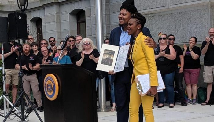 Two people standing side by side, holding document.