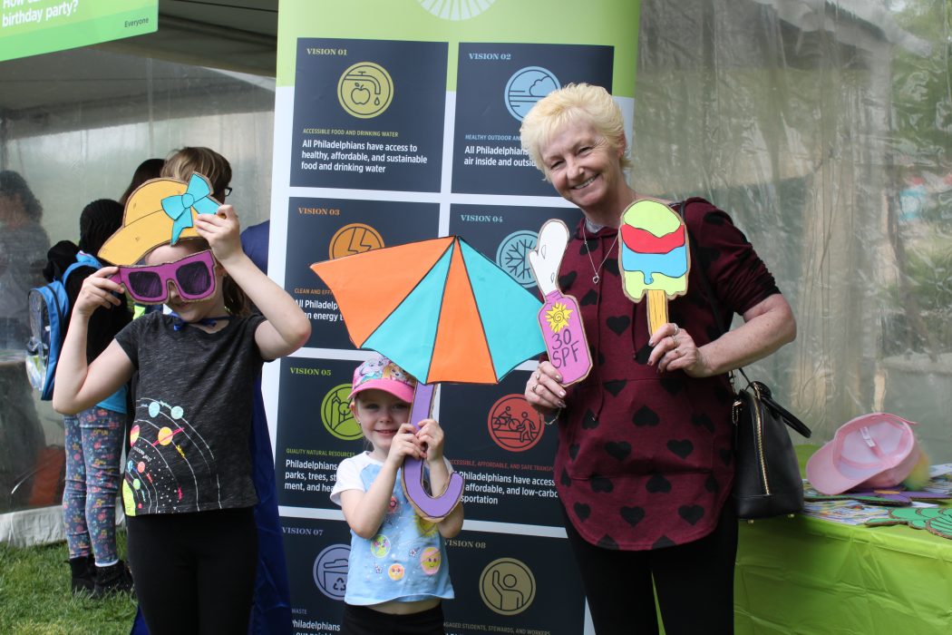 Two youth stand with their grandmother holding sun hat, parasol, and ice cream props from the Beat the Heat station at the 2019 Science Festival Carnival