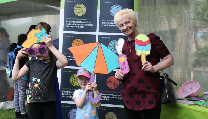 Two youth stand with their grandmother holding sun hat, parasol, and ice cream props from the Beat the Heat station at the 2019 Science Festival Carnival