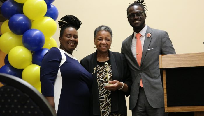 Alain Locke Community Schools Coordinator Pam Evans, award recipient Reverend Phyllis Harris, and Community Schools Director of Operations Maxwell Akuamoah-Boateng smiling during the Community School Award Ceremony. Reverend Harris proudly holds her Community Schools champion trophy in her hands.