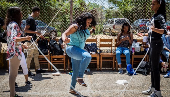 Two students stand across from each other, while a student in the middle of them jumps rope they are swinging