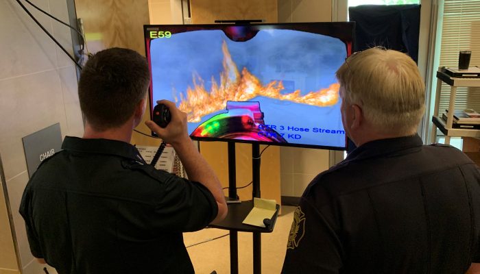 Two men look at a screen showing a simulated fire.