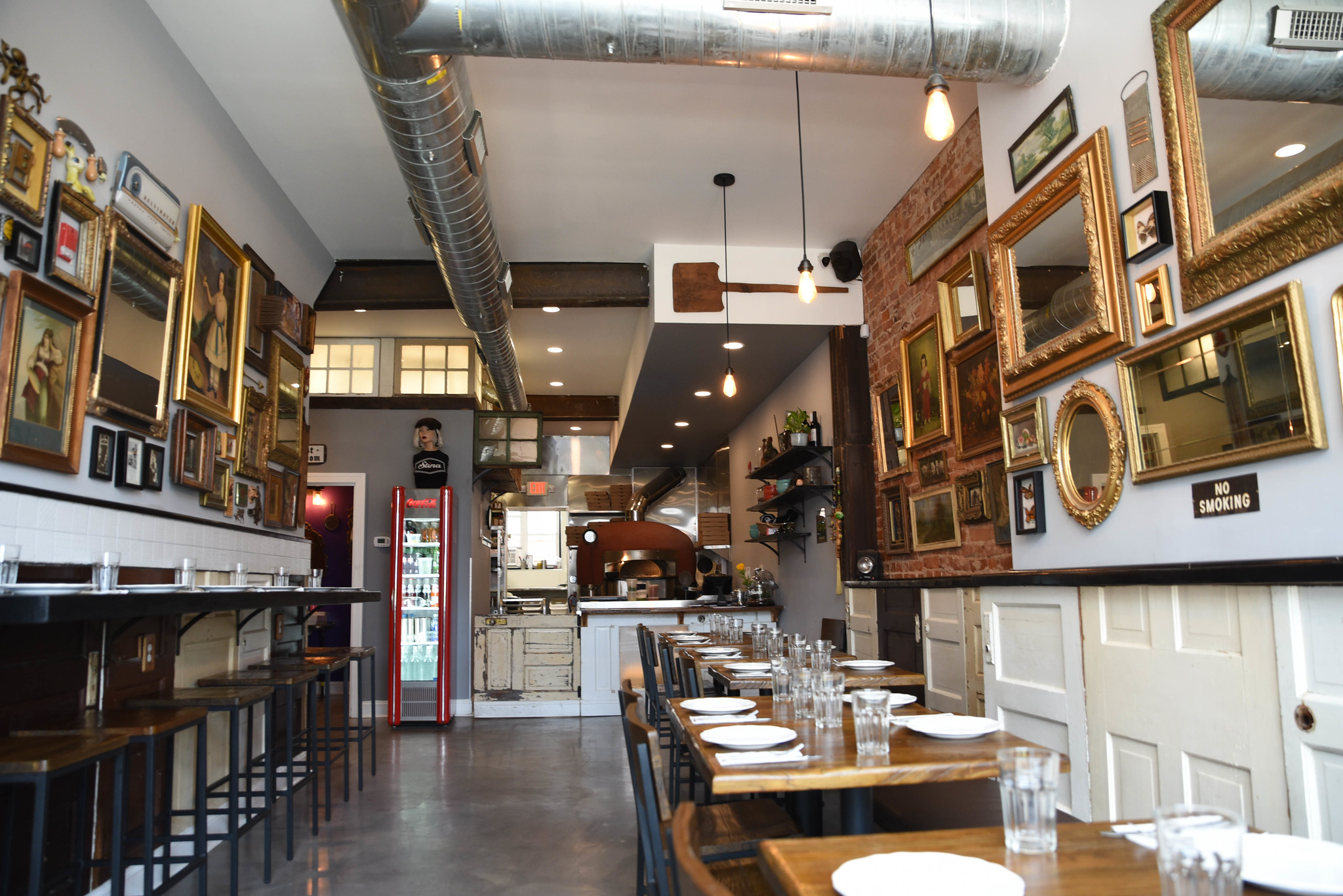 The interior of Stina. Bar-style seating is on the left side of the restaurant, tables on the right, and a counter straight ahead. A all of the restaurants walls are decorated with a gallery-style display of artwork.