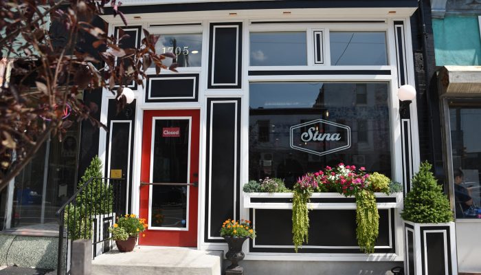 The exterior of Stina. The storefront features new windows, fresh paint, flowers in planters, a freshly-paved sidewalk, and more.
