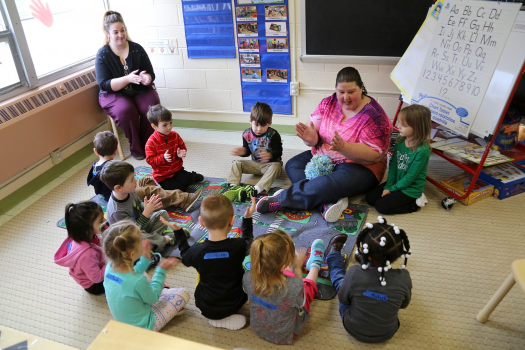 PHLpreK teacher Patty siting on the floor smiling and clapping with students.