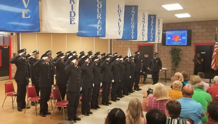 Twenty-seven paramedics in dress uniform saluting.