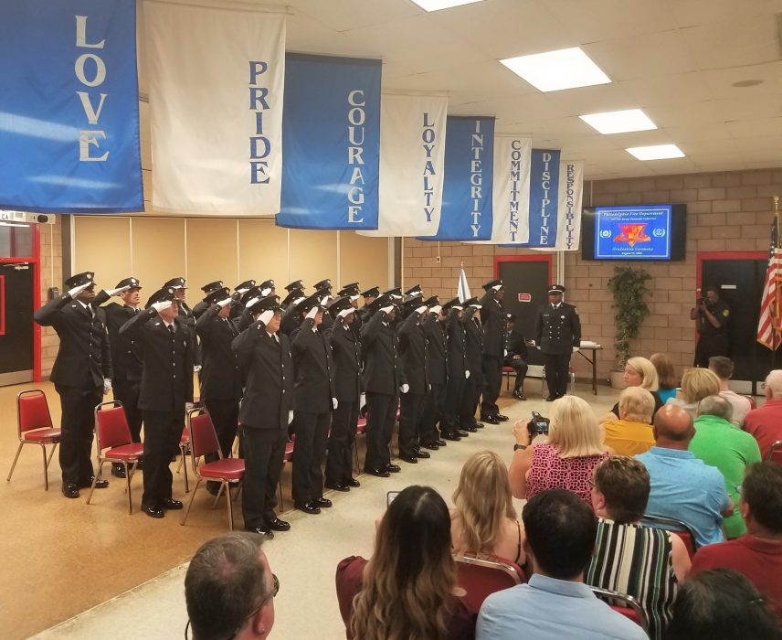 Twenty-seven paramedics in dress uniform saluting.