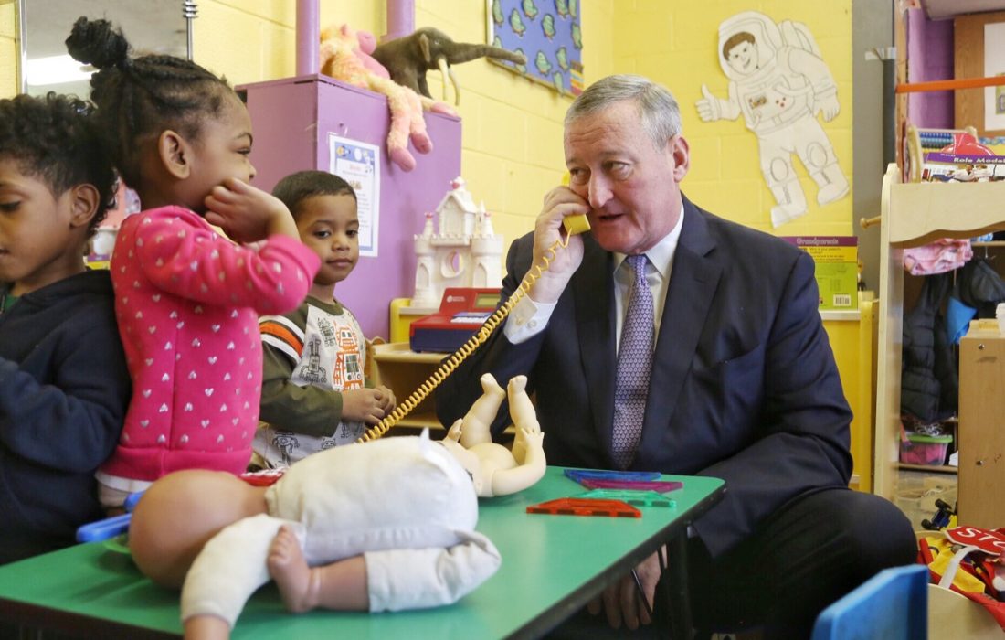 Mayor Kenney speaking on a toy phone while PHLpreK students look on.