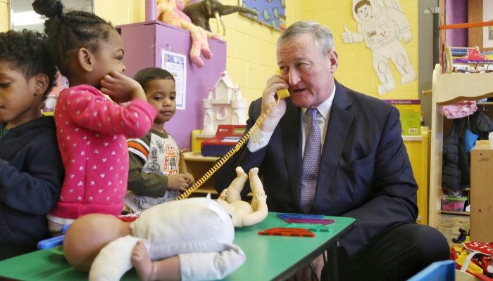 Mayor Kenney speaking on a toy phone while PHLpreK students look on.