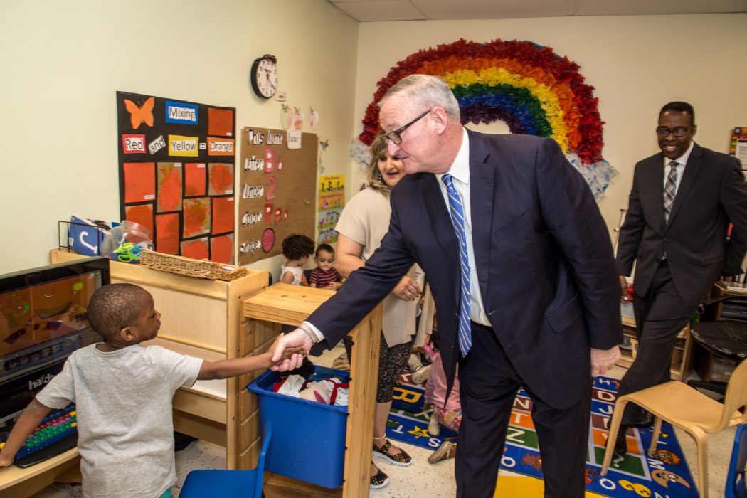 Mayor Kenney shaking hands with a PHLpreK student inside a classroom at Drueding Center. A brightly colored rainbow is on the wall behind them.