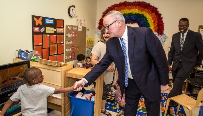 Mayor Kenney shaking hands with a PHLpreK student inside a classroom at Drueding Center. A brightly colored rainbow is on the wall behind them.