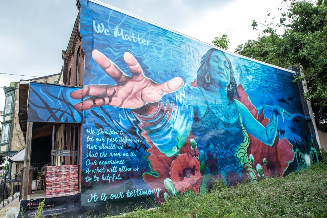 A mural in West Philly that shows a picture of a resilient woman reaching out, with the words, "We matter. We shouldn't let our past define us," as part of an inspirational poem.
